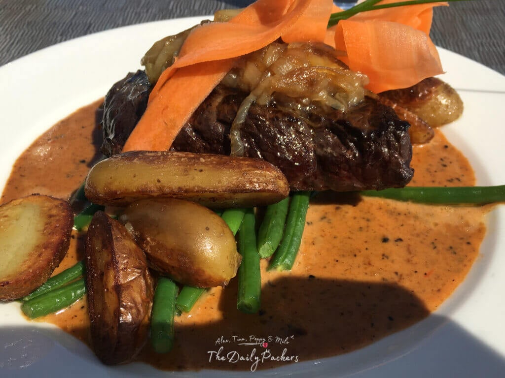 Whale steak served with roasted potatoes, green beans, carrot ribbons, and a rich peppercorn sauce on a white plate.
