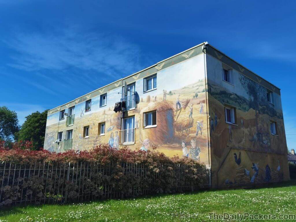 Residential building in the Bel Air neighborhood of Chartres with an entire facade painted as a countryside harvest scene under a clear blue sky