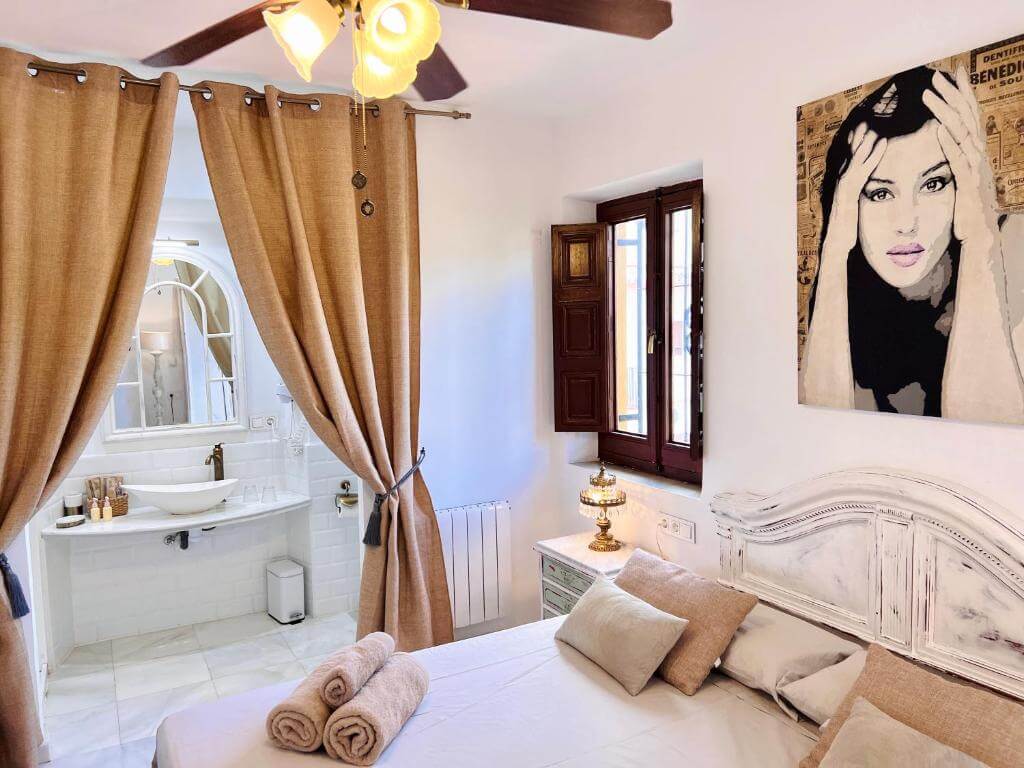Charming boutique room at Hotelito Suecia in Granada with warm earthy tones, a vintage lamp, and a cozy ensuite bathroom behind curtains.