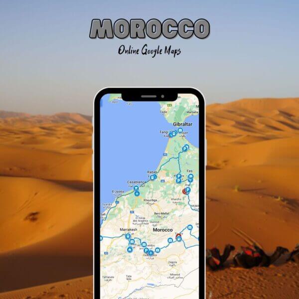 Téléphone portable montrant notre carte Google du Maroc avec des épingles de voyage à travers le pays, placé devant des dunes de désert et des chameaux se reposant dans le sable.