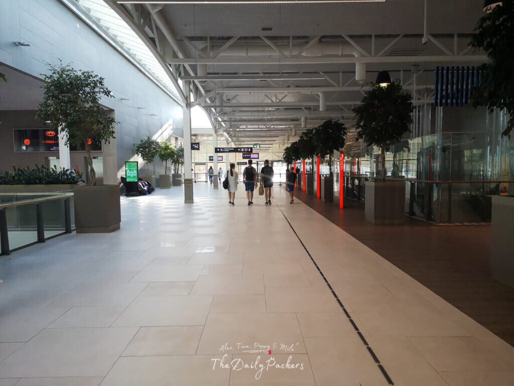 Interior of the Tallinn ferry terminal with wide tiled walkways, shops, and travelers walking toward the gates