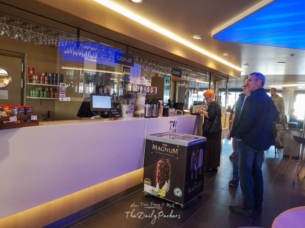 Passengers waiting at the ferry bar counter with drinks, snacks, and a Magnum ice cream freezer