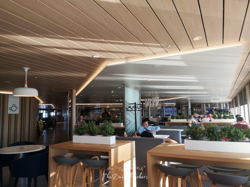 Stylish ferry lounge with wooden ceilings, modern decor, and passengers seated in booths by large windows