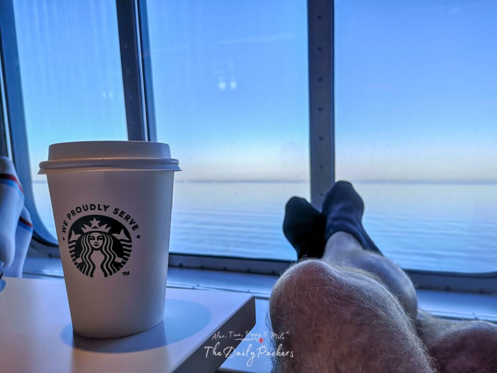 Cup of Starbucks coffee on a ferry table with relaxed legs and a calm sea view through the window
