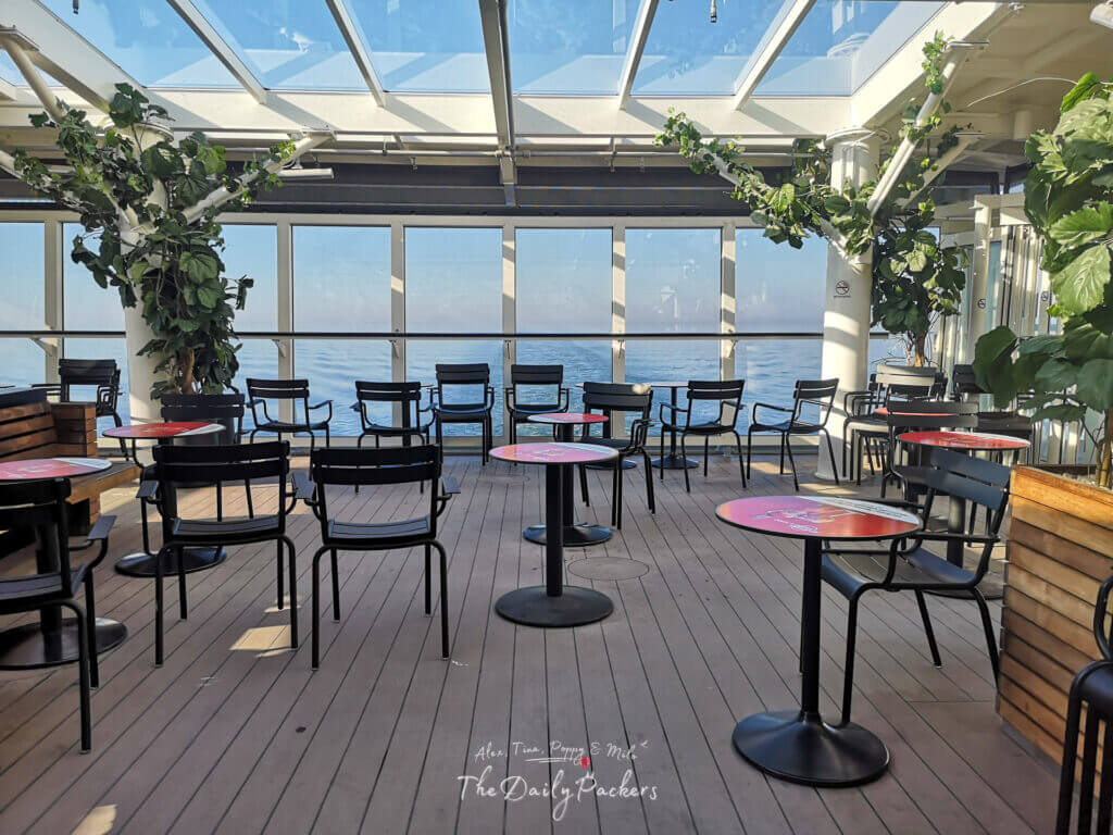 Sunny ferry rear lounge with ocean views, glass ceiling, wooden deck, and empty black chairs