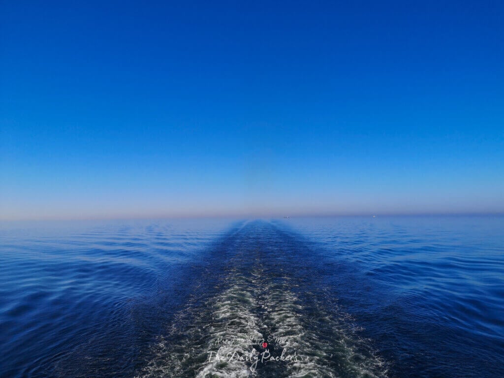 Endless sea horizon and ferry wake trail under a vibrant blue sky, viewed from the rear deck