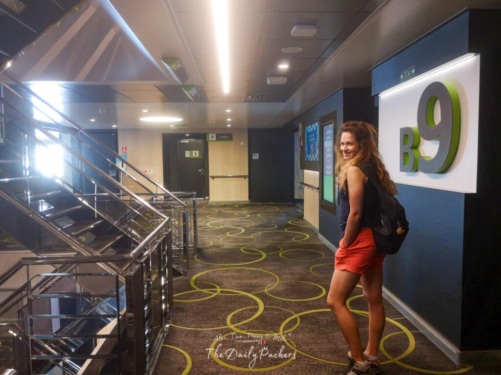 Woman smiling in a modern ferry corridor near staircase B9, with patterned carpet and signage