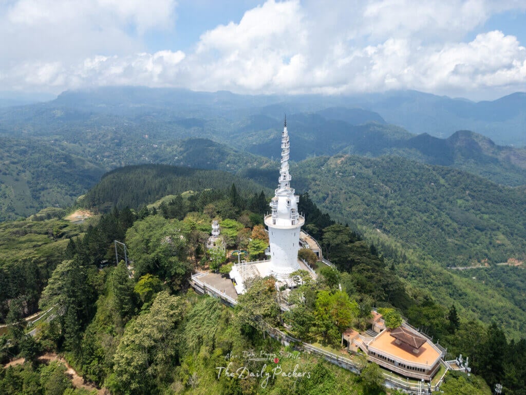 Prise de vue par drone de la tour d'Ambuluwawa entourée de forêts et de collines au Sri Lanka sous un ciel partiellement nuageux.