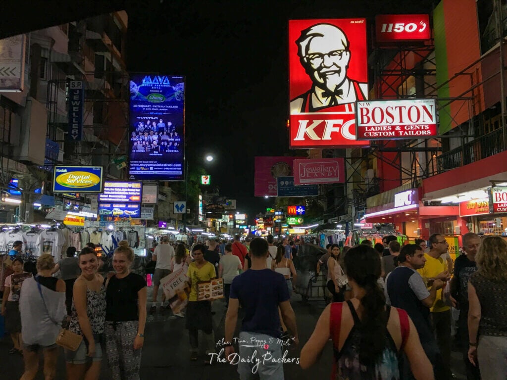 Crowded Khao San Road in Bangkok at night with bright neon signs, street vendors, and tourists.