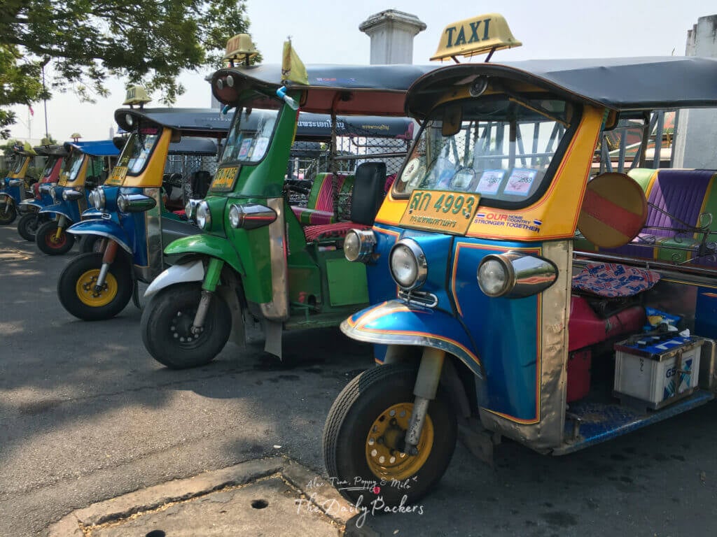 Line of colorful tuk-tuks parked along the roadside in Bangkok waiting for passengers.