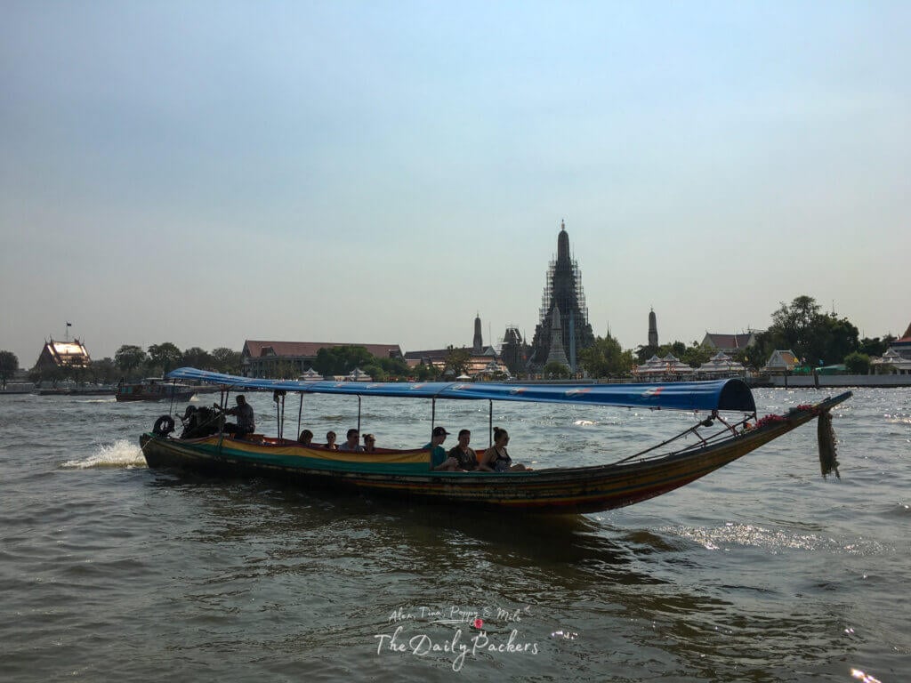 Longtail boat carrying tourists along the Chao Phraya River with temple spires in the background.