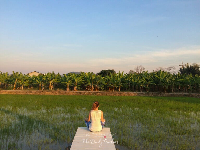 Woman sitting at the edge of a wooden walkway overlooking rice paddies and banana trees in Chiang Rai in Northern Thailand