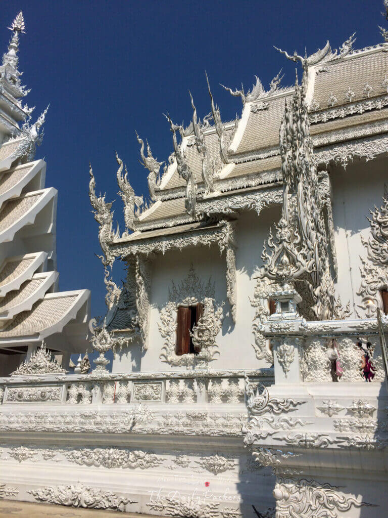 Gros plan sur les sculptures blanches complexes et les détails en miroir du temple blanc sous un ciel bleu profond à Chiang Rai.