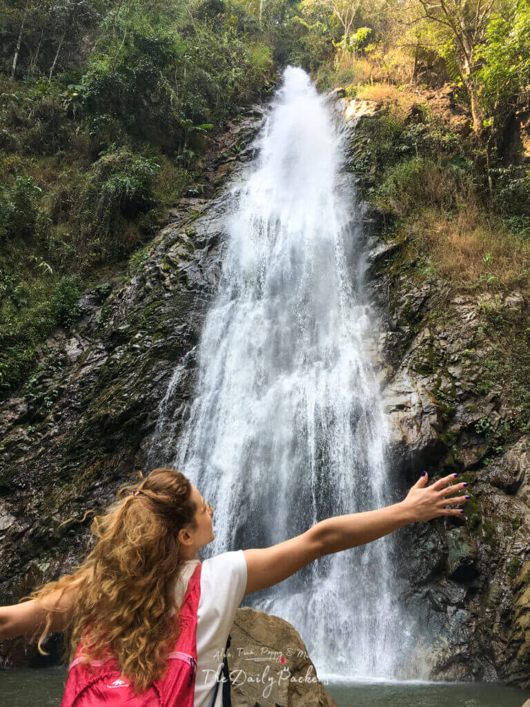 Femme aux bras ouverts devant la puissante cascade de Khun Korn entourée de forêt à Chiang Rai, Thaïlande.
