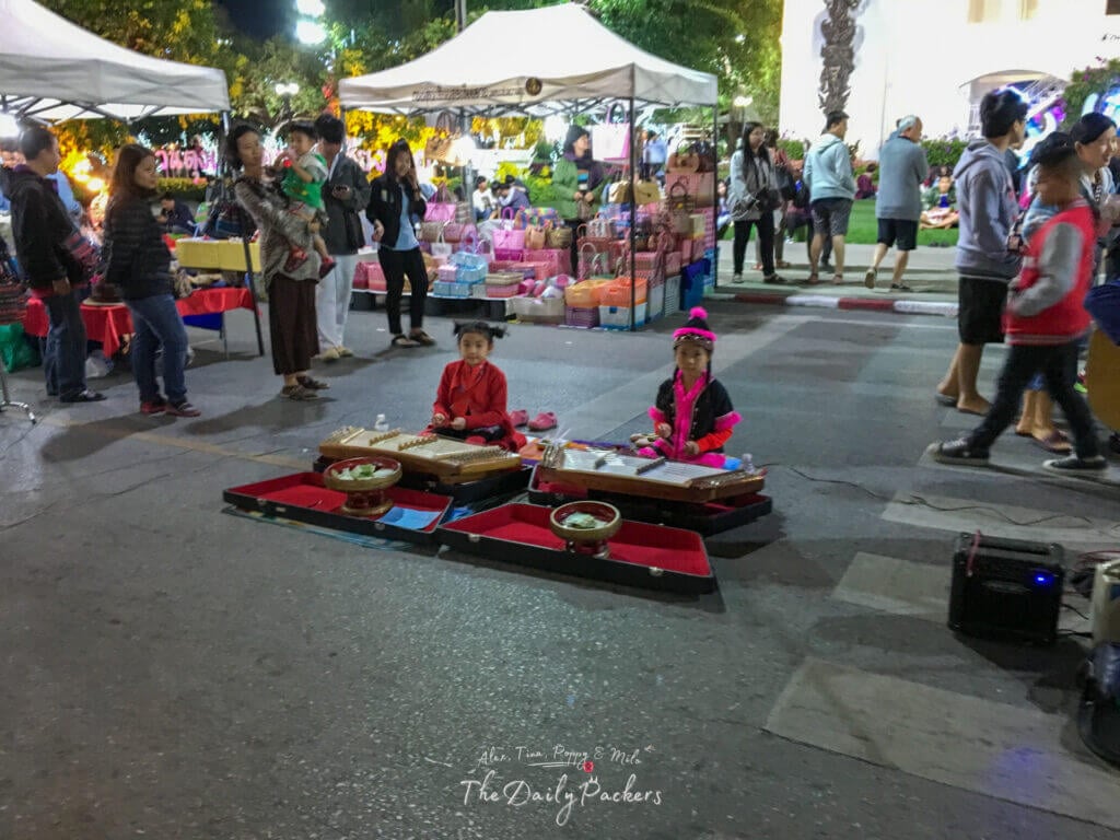 Deux jeunes filles en tenue traditionnelle jouant d'instruments thaïlandais au marché de nuit de Chiang Rai