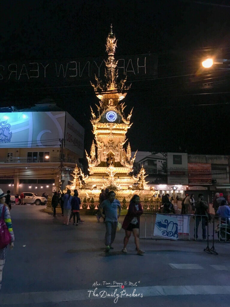 Tour de l'horloge dorée de Chiang Rai illuminée la nuit avec des gens marchant autour du rond-point.