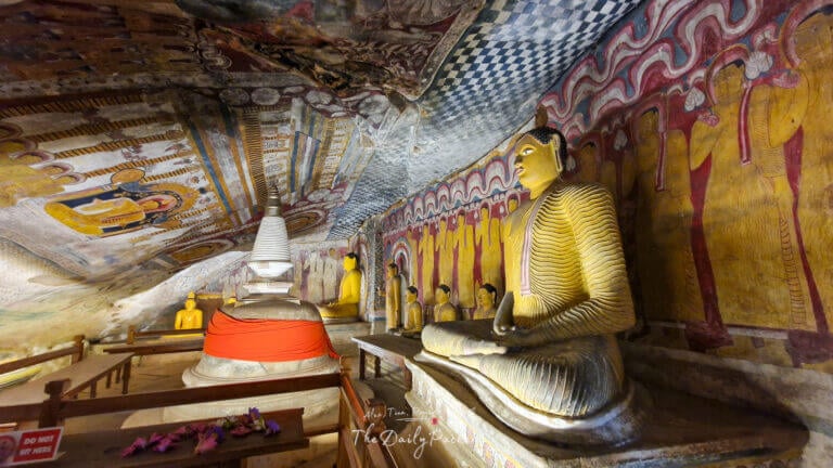 Intérieur de Temple troglodyte de Rangiri Dambulla avec des peintures murales colorées et des statues de Bouddha dorées assises en position de méditation à côté d'un stupa blanc.