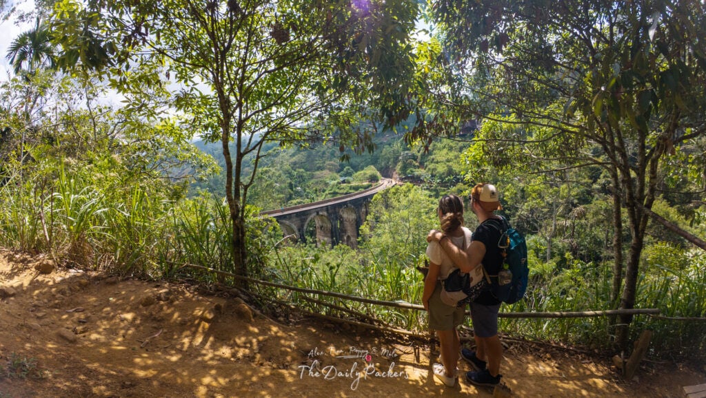 Couple standing together on a forested trail overlooking the Nine Arch Bridge in Ella