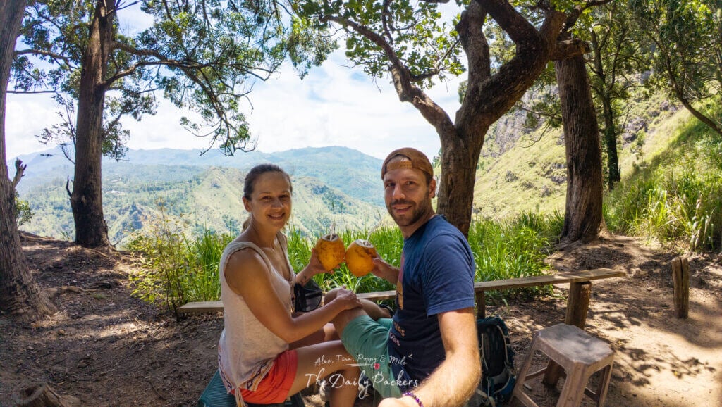 Couple faisant une pause coco le long du sentier de randonnée ombragé d'Ella Rock avec vue sur les montagnes.