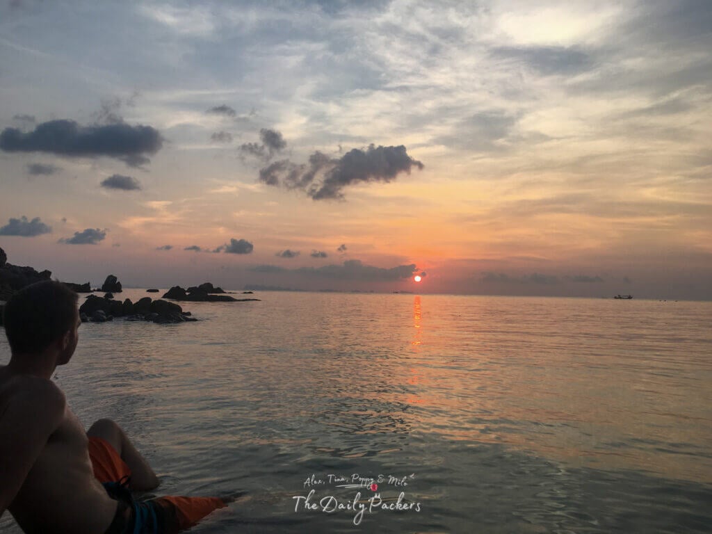 View of Bottle Beach on Koh Pha Ngan with lush green hills, turquoise water, and a white sandy shoreline framed by tropical trees.