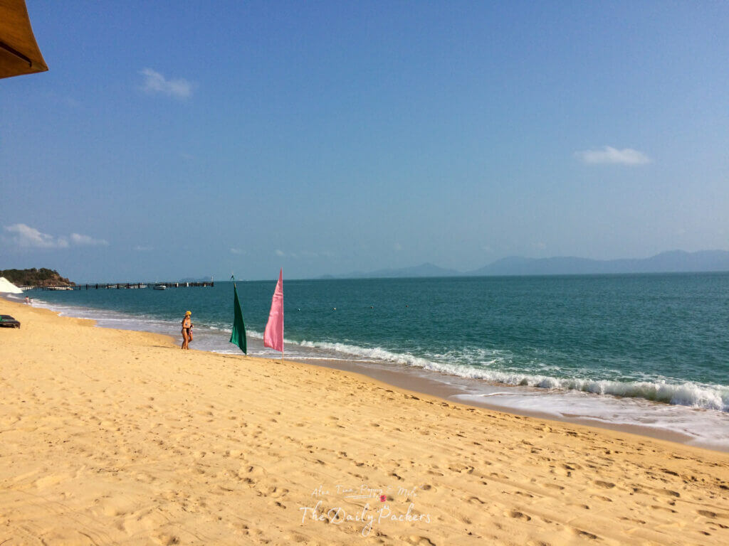 Wide view of an empty tropical beach with a woman walking near the waves under a clear sky.