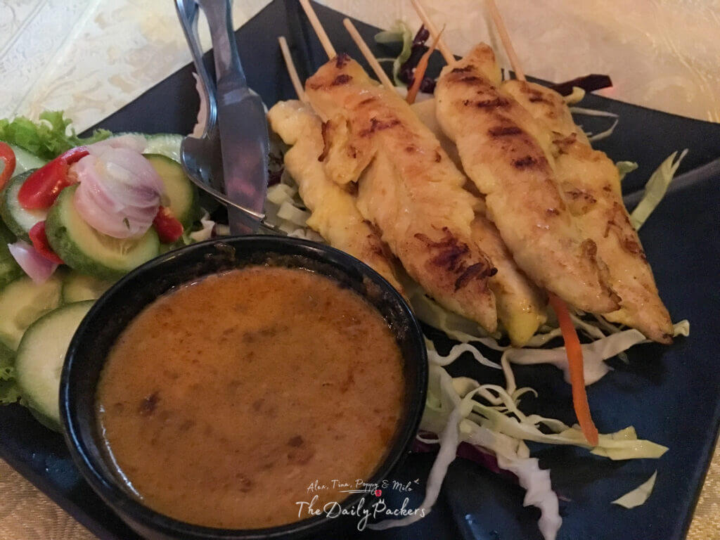 Thai-style satay skewers served with peanut sauce, cucumber salad, and shredded cabbage on a black plate