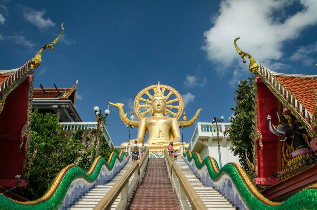 Big golden Buddha statue at Wat Phra Yai on Koh Samui with a grand staircase and ornate details under a bright blue sky