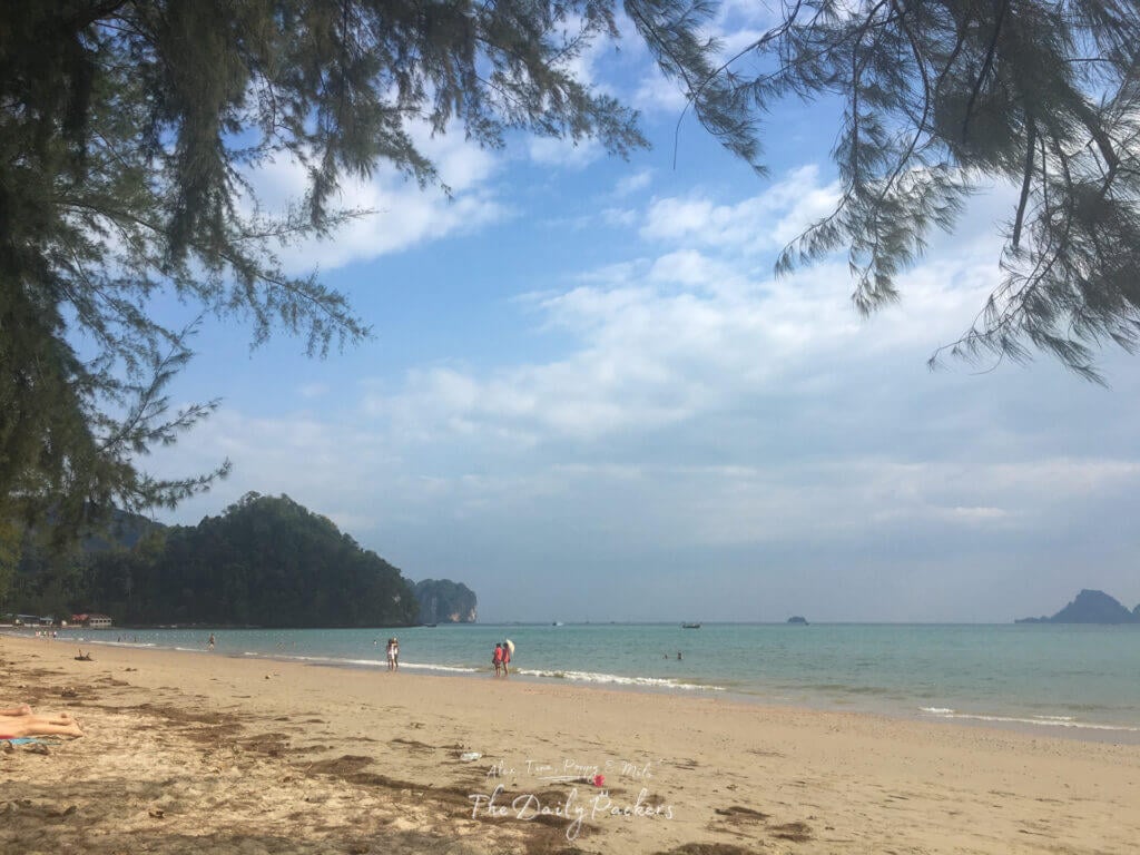 Golden sunset over Phra Nang Cave Beach in Krabi, Thailand with silhouettes of people walking along the shoreline and distant limestone islands.