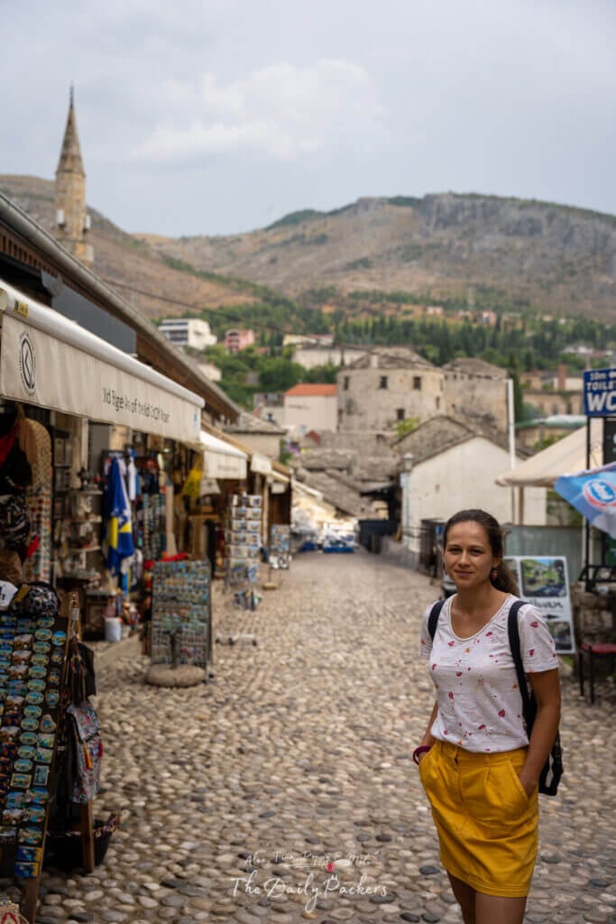Femme marchant dans les rues pavées du bazar de Mostar, bordé de boutiques de souvenirs et d'artisanat.