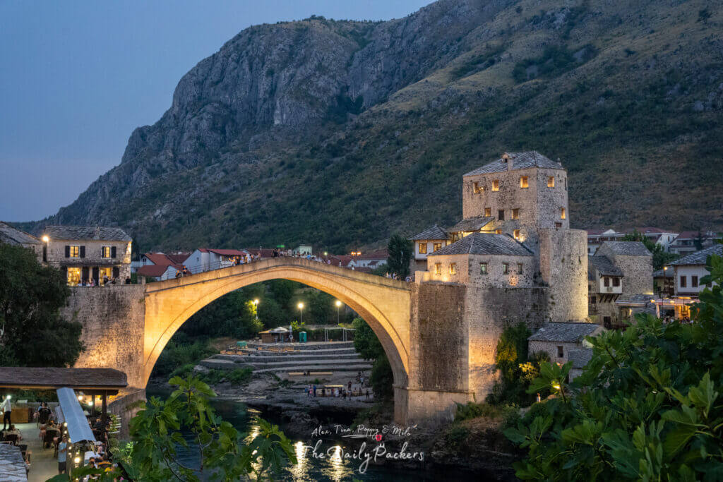 Le pont de Stari Most, illuminé d'or, enjambe la rivière Neretva et des cafés animés se trouvent au bord de l'eau à l'heure bleue.