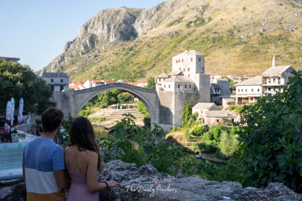 Couple regardant le vieux pont de Mostar depuis une terrasse en pierre surplombant la rivière.