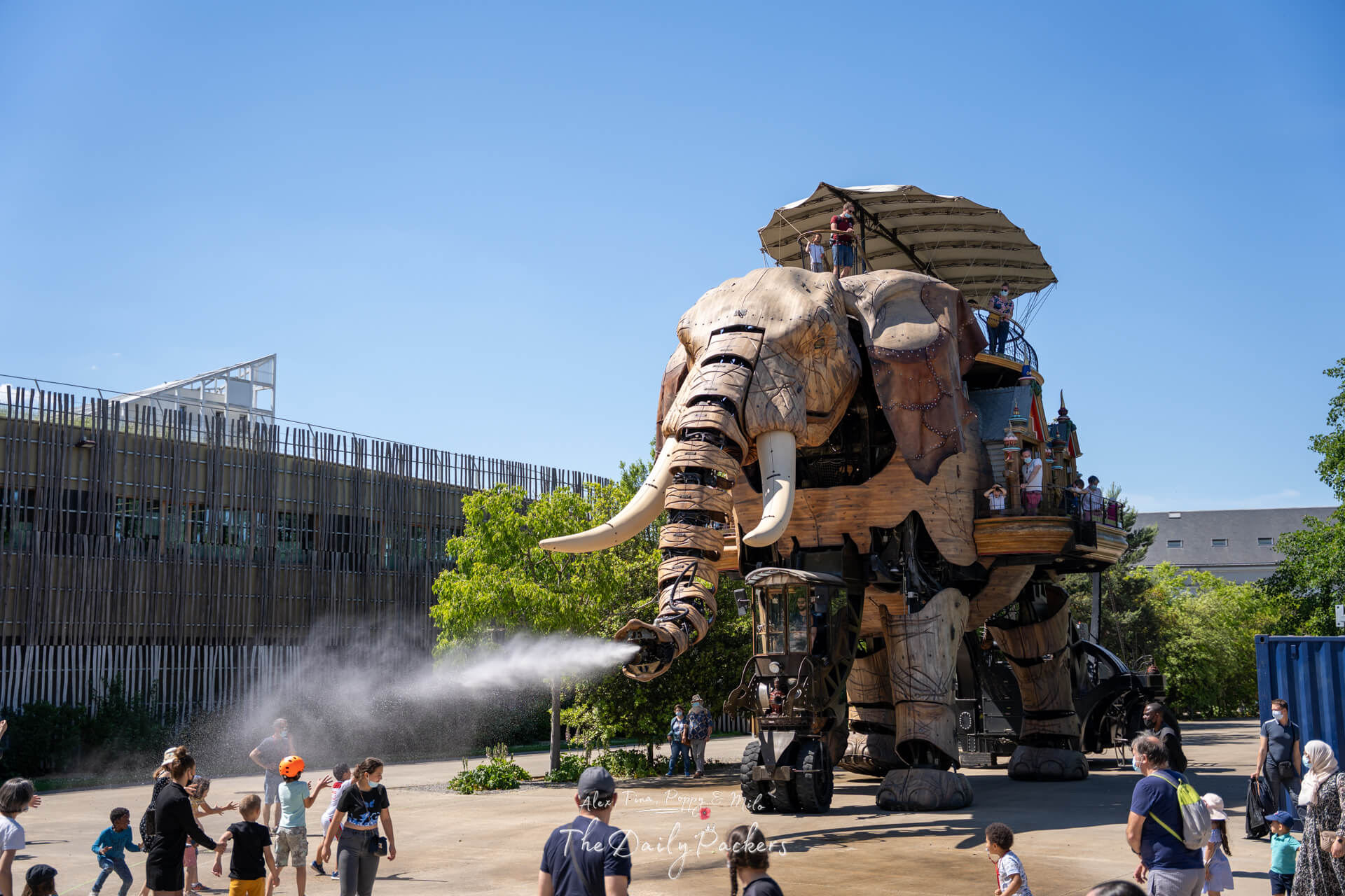 Close-up of the mechanical elephant spraying water while partially hidden behind green trees in Nantes.