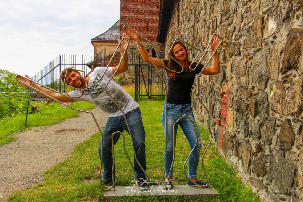 Des voyageurs posent de manière ludique avec des personnages en fil de fer devant la forteresse d'Akershus à Oslo.