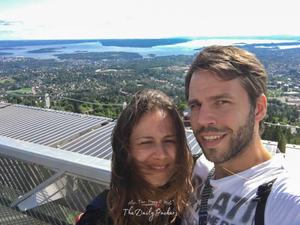 Couple souriant avec vue panoramique sur le fjord d'Oslo depuis le tremplin de saut à ski de Holmenkollen.