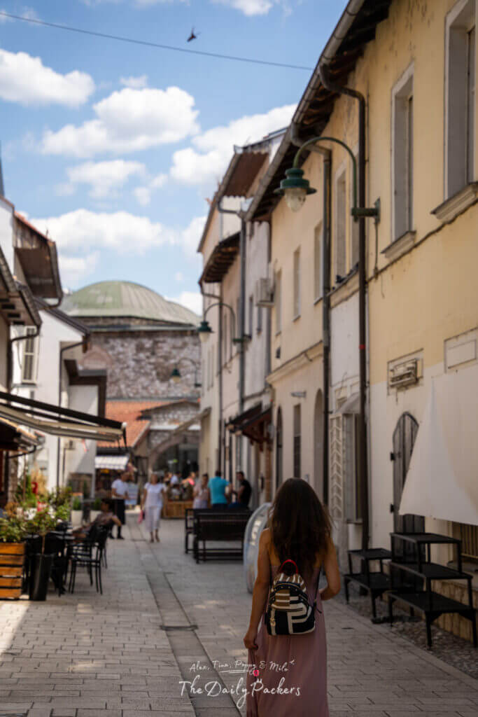 Femme explorant une charmante ruelle de la vieille ville de Sarajevo, avec ses bâtiments blanchis à la chaux et ses pavés.