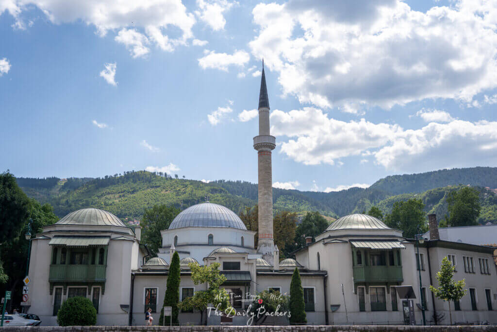 La mosquée de l'Empereur de Sarajevo, avec son élégant minaret et ses toits en dôme, est entourée de collines et de verdure.