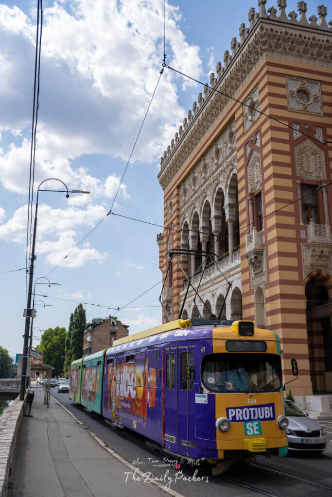 Tramway coloré passant devant l'hôtel de ville de Sarajevo, un bâtiment historique austro-hongrois.