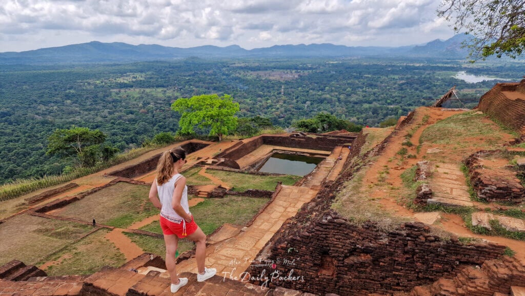 Vue des ruines de la forteresse de Sigiriya avec une femme marchant sur les anciens chemins de pierre surplombant la jungle.
