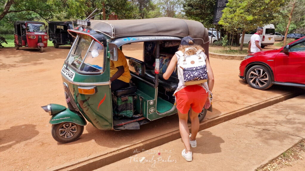 Woman boarding a green tuk-tuk outside the Sigiriya archaeological site on a sunny day