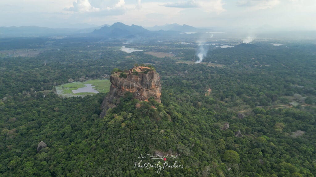 Vue large par drone du rocher de Sigiriya dans la campagne sri-lankaise avec des collines brumeuses en arrière-plan.