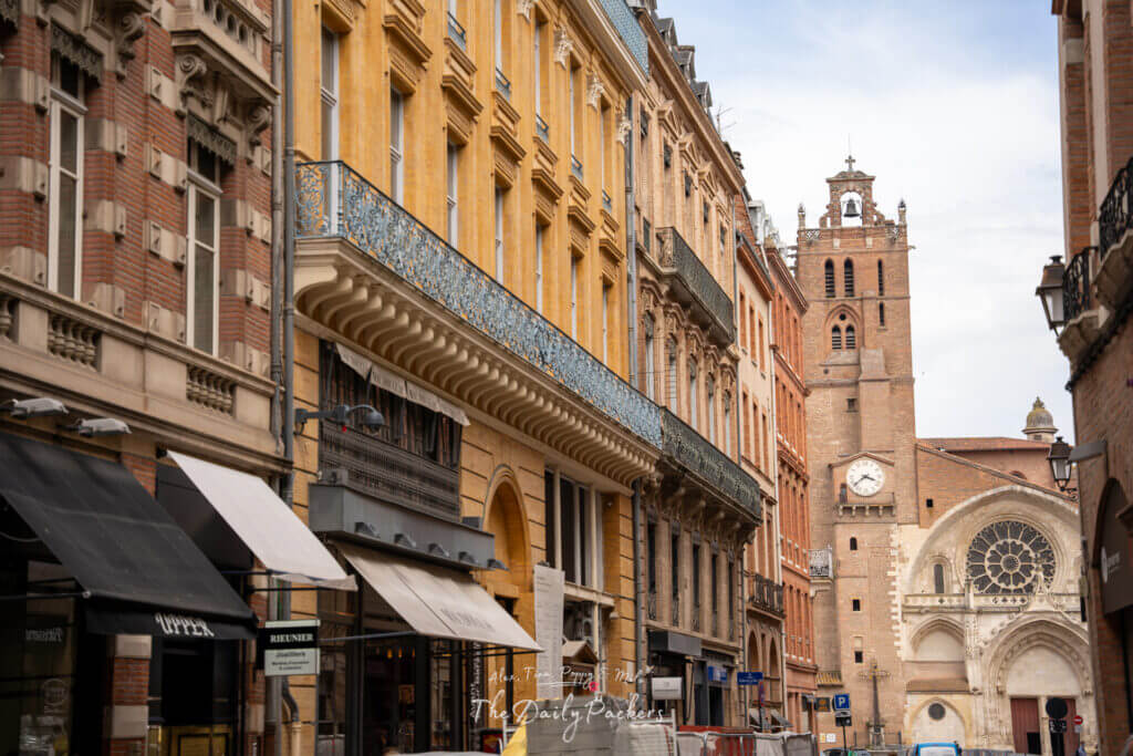 Vue de la rue menant à la cathédrale de Toulouse, bordée de bâtiments historiques colorés.