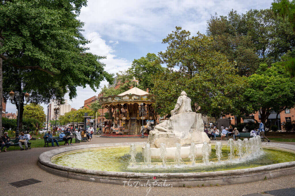 Wilson Square in Toulouse featuring a large fountain and a classic carousel surrounded by trees.