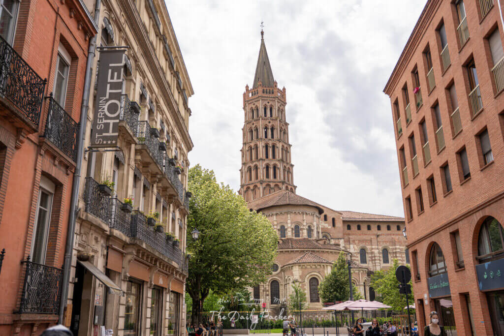 Street view of the Basilica of Saint-Sernin with its distinctive bell tower framed by buildings.