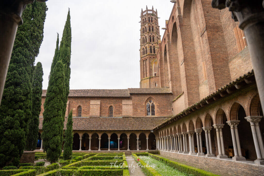 Cloister of the Jacobins Convent with manicured hedges, tall cypress trees, and Gothic arches.