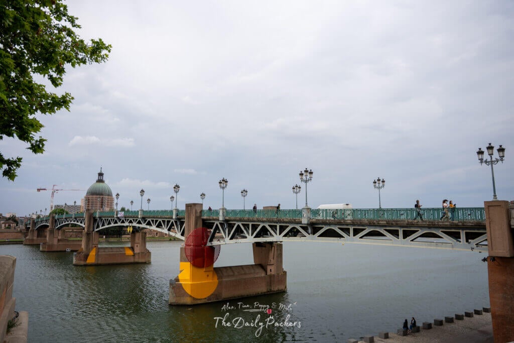 Pont Saint-Pierre bridge spanning the Garonne River with people walking and the dome of La Grave in the background.