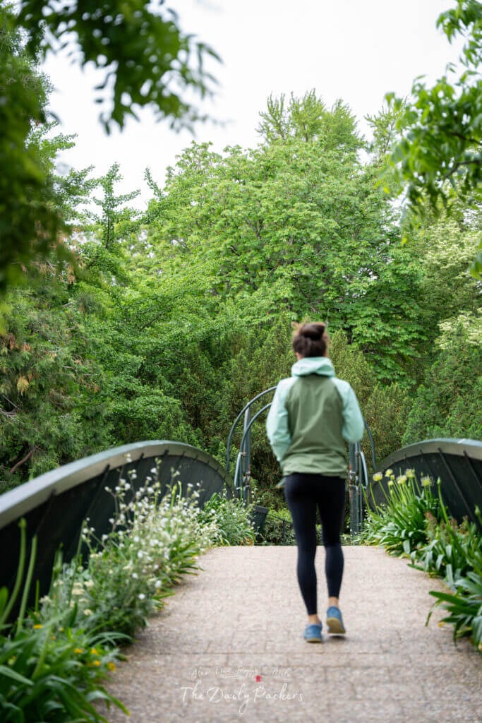 Woman walking on a garden bridge surrounded by lush greenery in Toulouse’s Jardin des Plantes.