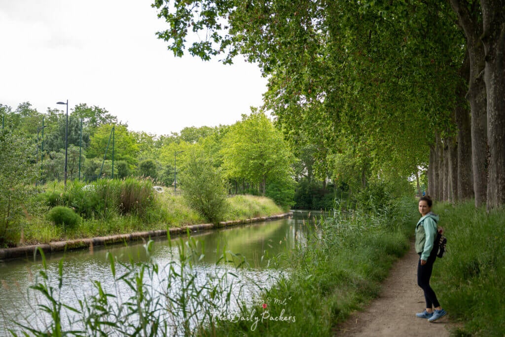 Smiling woman looking back while walking along the tranquil, tree-lined Canal du Midi path.