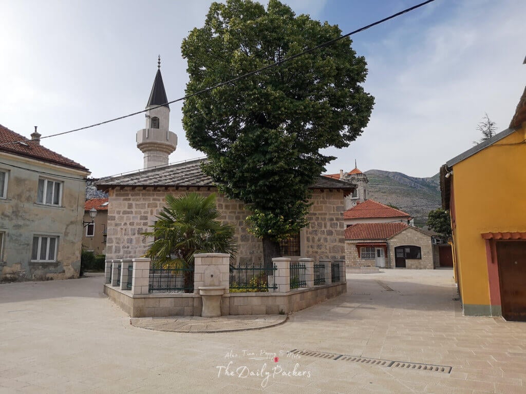 Small mosque with a minaret and stone fountain surrounded by colorful houses in Trebinje’s old town.