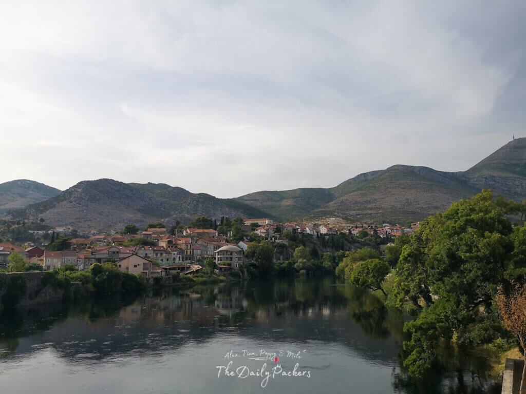 View over Trebinje’s rooftops and lush greenery with mountains in the background on a cloudy afternoon.