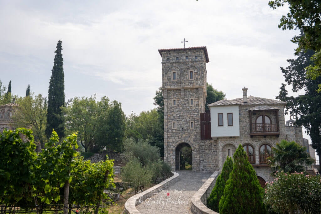 Entrance to Tvrdoš Monastery, with a stone tower and traditional architecture surrounded by trees and a vineyard path.